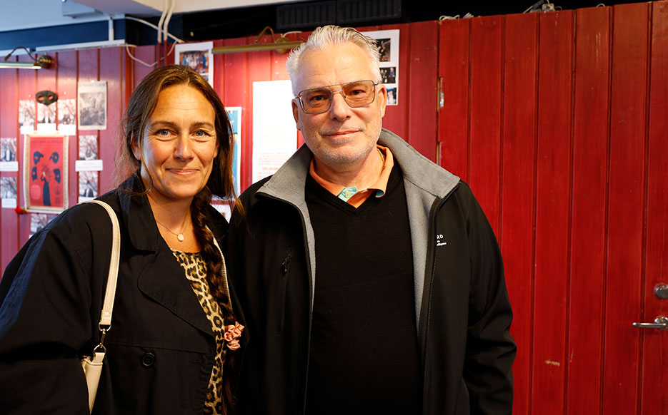 En man och en kvinna i medelåldern ler mot kameran. I bakgrunden syns en röd vägg.