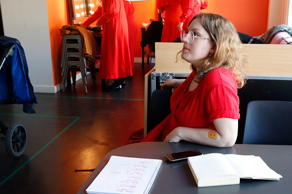 Amanda sitter sidledes i en stol och tittar upp på någon utanför bild. Framför henne ligger ett block där en setlista står skriven med lila penna.