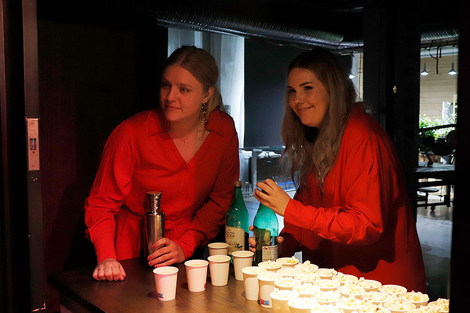 Sara och Gabriella står lutade över en liten bardisk och häller upp cider i små pappersmuggar.